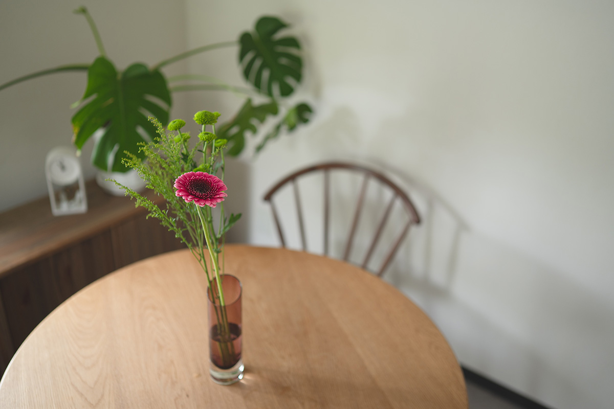 団地のダイニングテーブルに飾った一輪挿しのガーベラと観葉植物。木の椅子と白い壁の明るい部屋