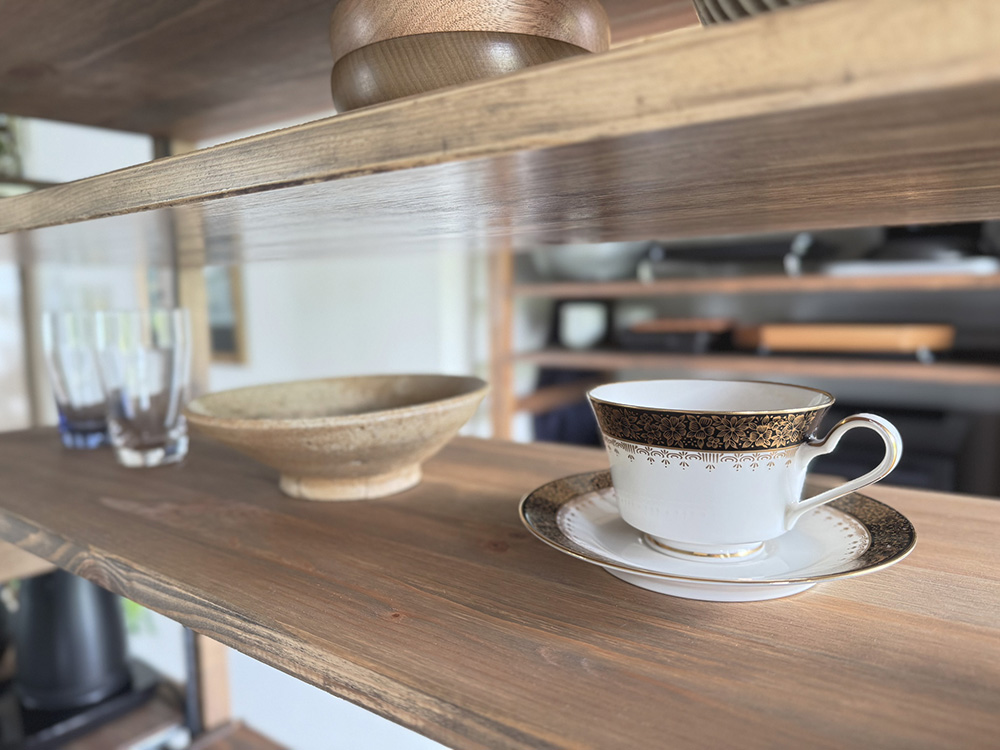 木製の飾り棚に金縁のカップ＆ソーサーや器をゆとりをもって飾ったディスプレイ。余白を生かした見せる収納