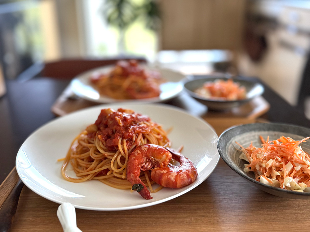 明るい窓辺のテーブルに盛り付けた海老のトマトパスタとサラダ。お気に入りの器で整えた食卓
