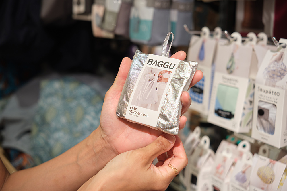 「BAGGU」などデザイン豊富なエコバッグのパッケージを持つ手元