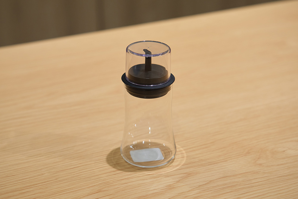 iwaki「フタ付醤油差し M」。木のテーブルに置いたガラス製しょうゆ差し